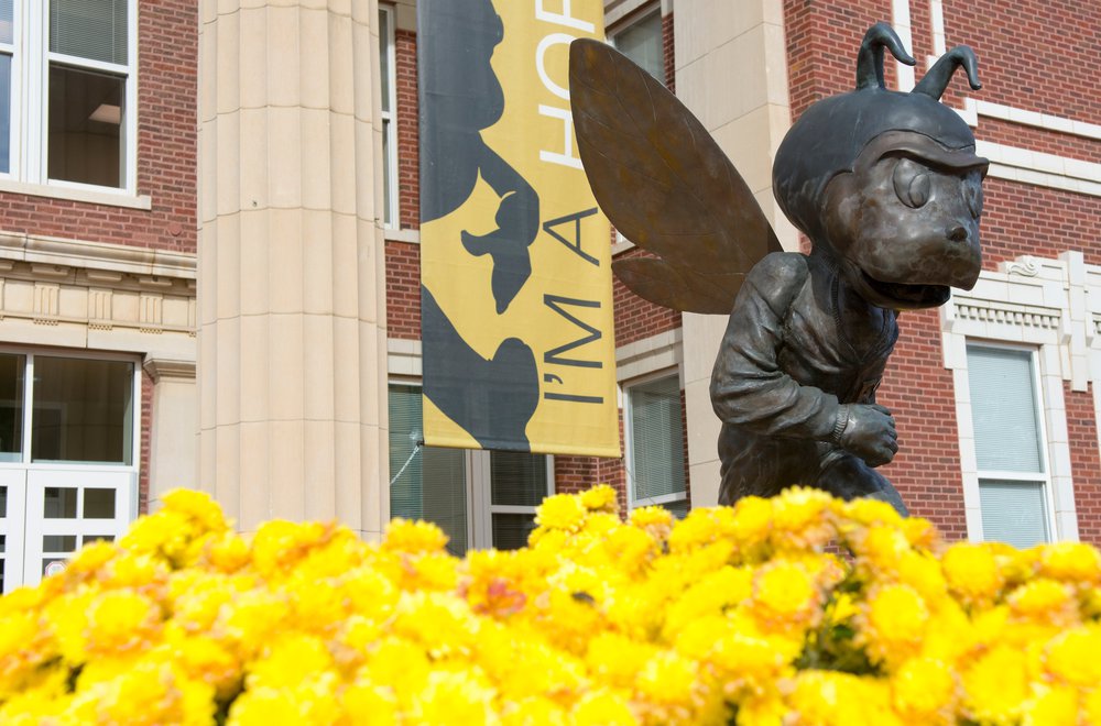 Bronze Corky in front of Plumb Hall surrounded by flowers