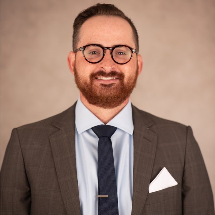 A head and shoulder photo of a man with beard and round glasses.