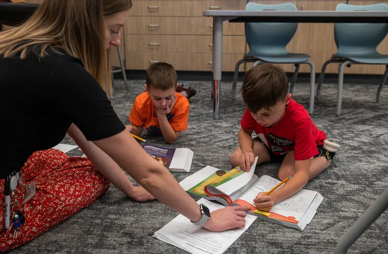 Two students reading a book with the help of a teacher