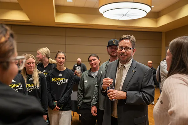 Man with beard talking with group of women, others.