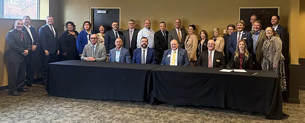 Group of men and women both seated at and standing behind an eight-feet-long table draped with a black cloth.