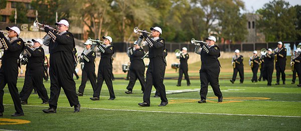 People playing trumpets walk in line on football field