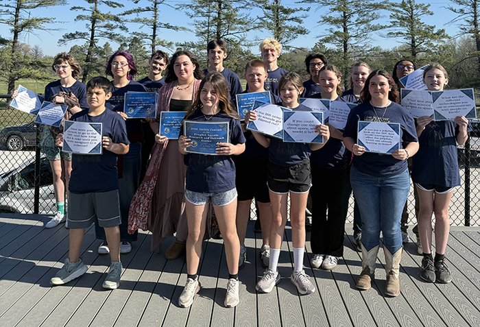 Group of students hold laminated cards that show the questions they asked an astronaut.