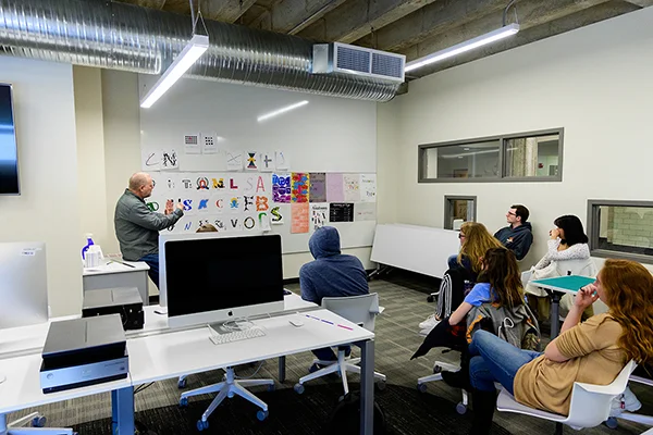 Students seated watching professor at white board demonstrating graphic design