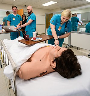 Two men and one women practice nursing techniques on mannequin in simulation lab.