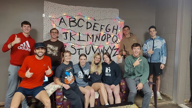Ten students sit on and stand around a couch.