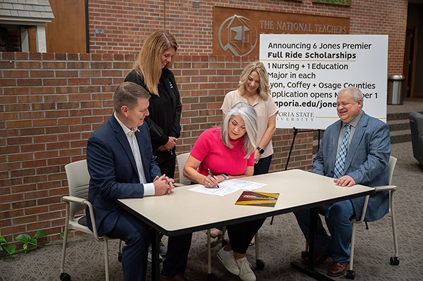 Womans signs paper at a table with two men and two other women.